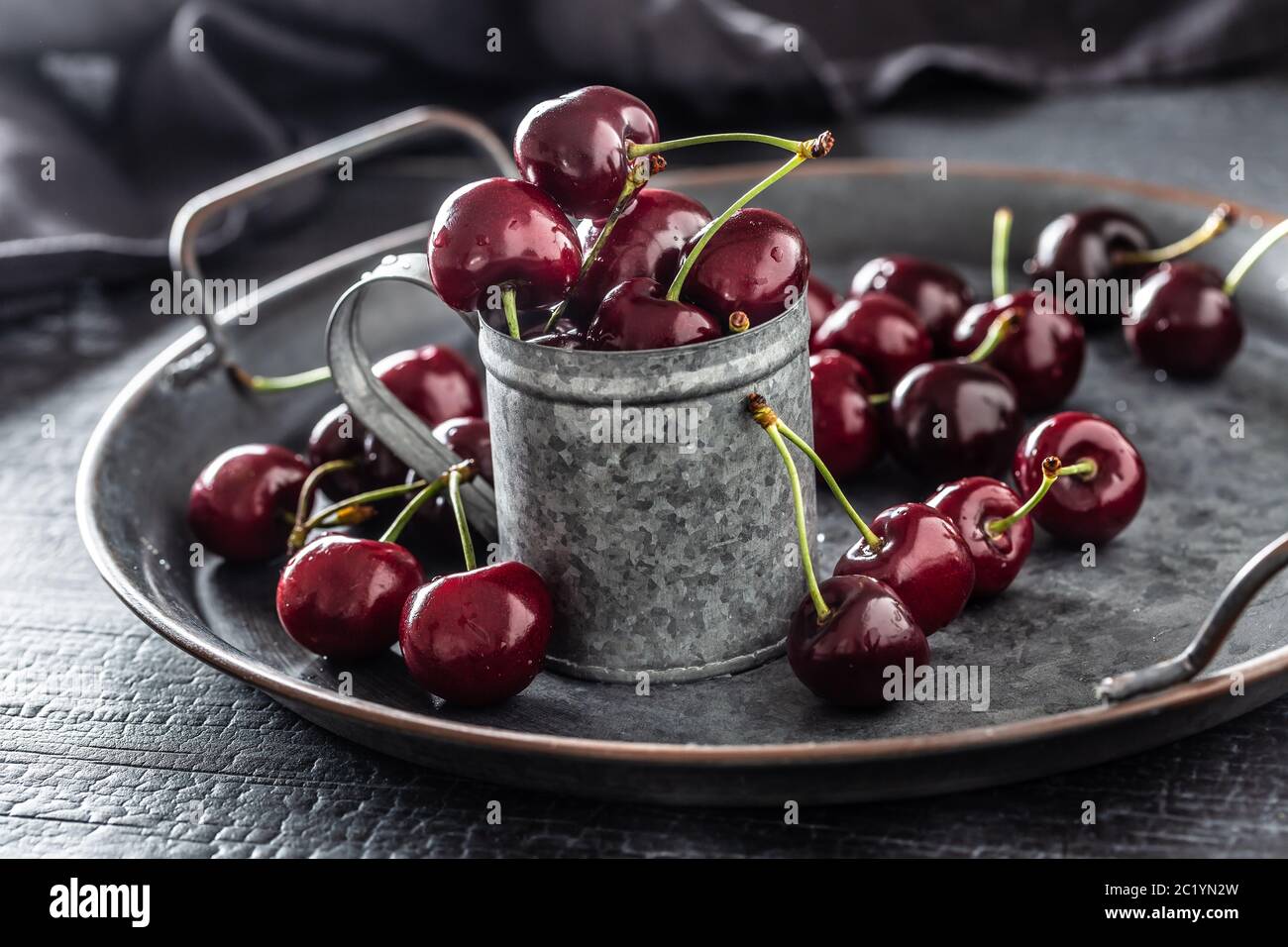 Vassoio vintage metallizzato, superficie e tazza con ciliegie rosse succose all'interno della tazza e sparse intorno al vassoio Foto Stock