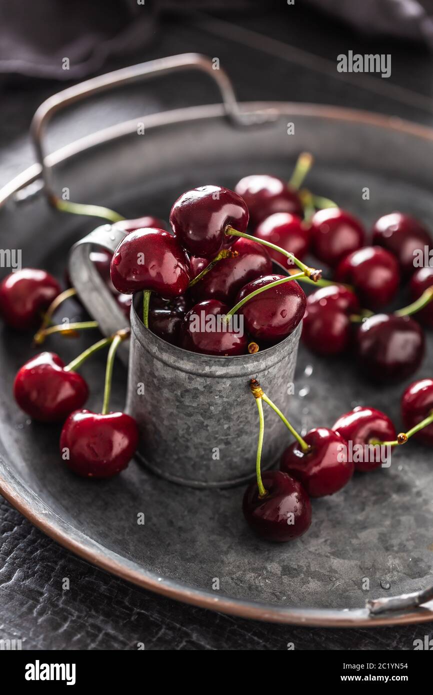 Vassoio vintage metallizzato, superficie e tazza con ciliegie rosse succose all'interno della tazza e sparse intorno al vassoio Foto Stock