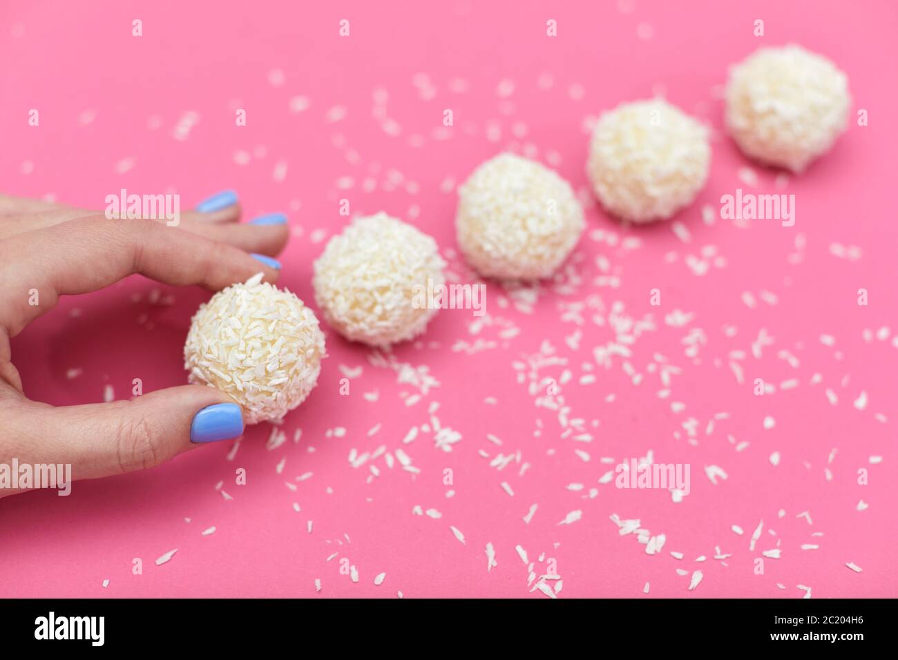 mano femminile con caramelle ricoperte di cocco grattugiato. palline di cocco su sfondo rosa Foto Stock