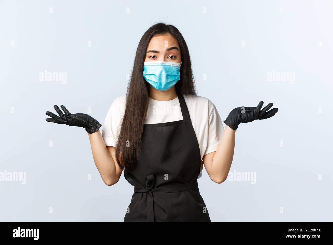 Covid-19, social distancing, piccola azienda di caffè e prevenzione virus concetto. Unware e senza clueless asiatico dipendente femminile in grembiule, maschera medica Foto Stock