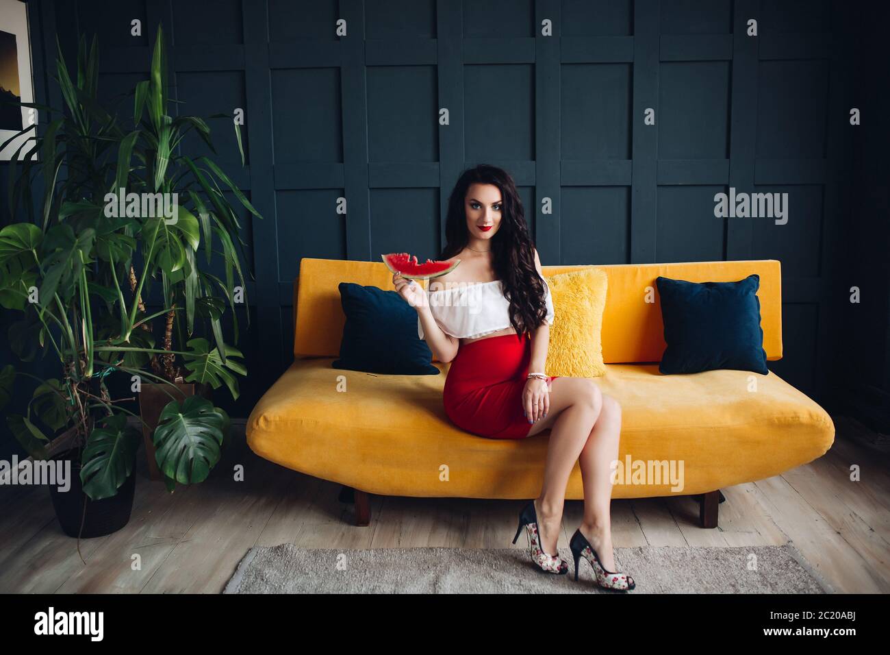 Elegante donna incinta seduta sul divano arancio e posa Foto Stock