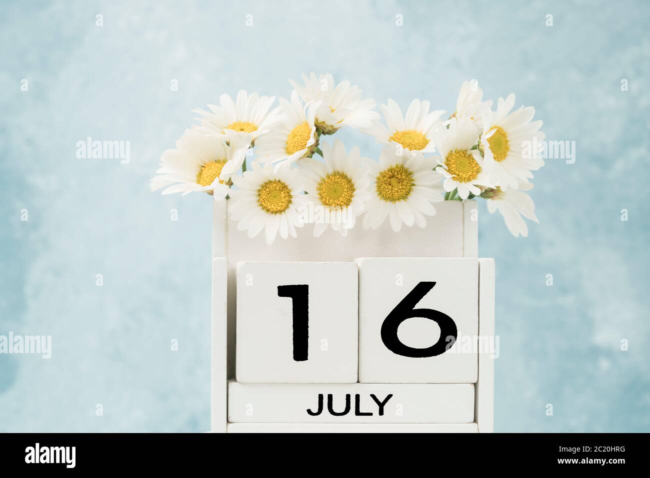 Calendario cubo bianco per luglio decorato con fiori margherita su blu con spazio copia Foto Stock