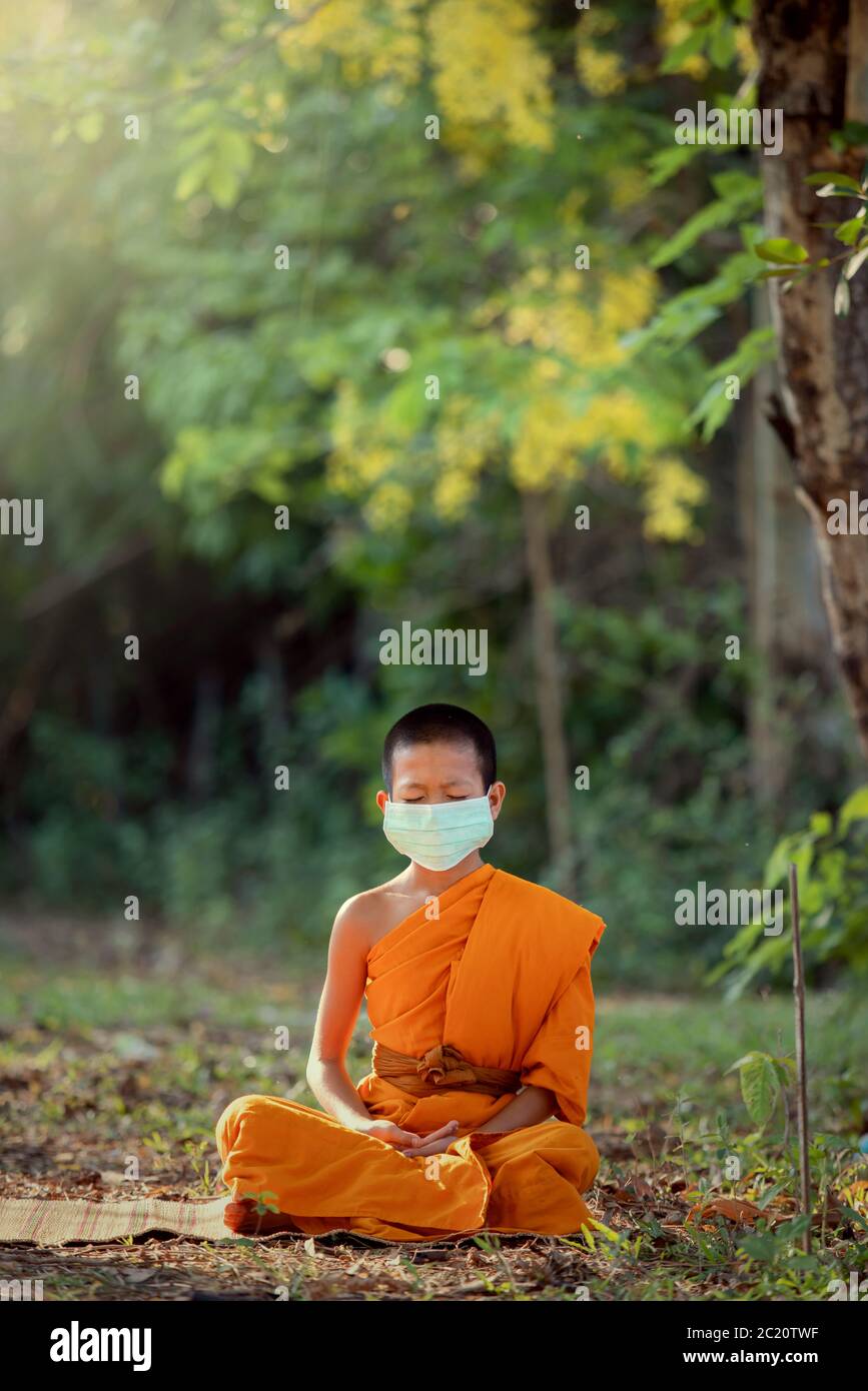 Novizio che indossa la meditazione maschera sotto un albero nel tempio con stile di vita nuovo normale Foto Stock