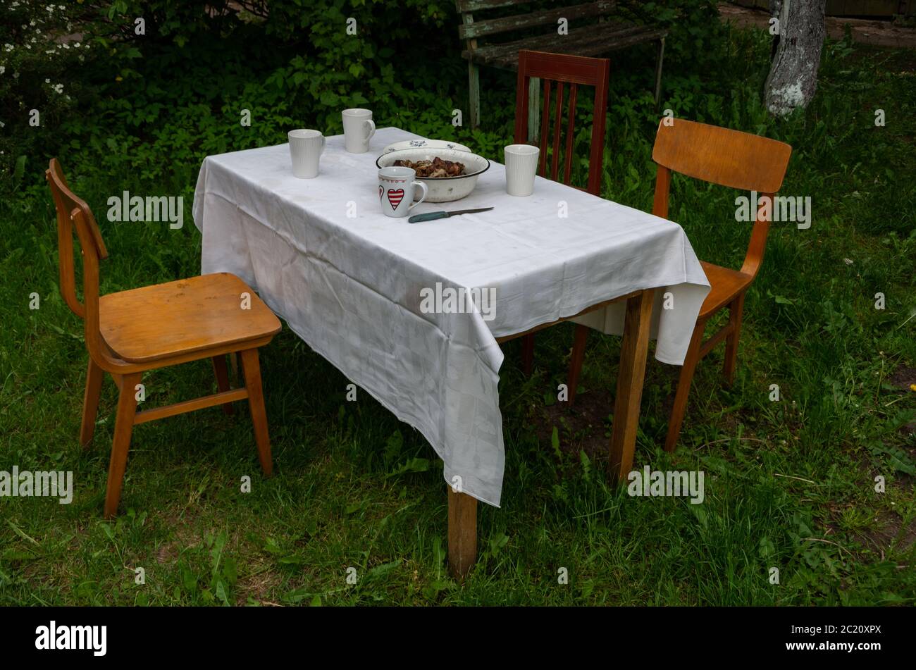 Tavolo esterno con tazze e carne e sedie vecchie, bianco Foto Stock