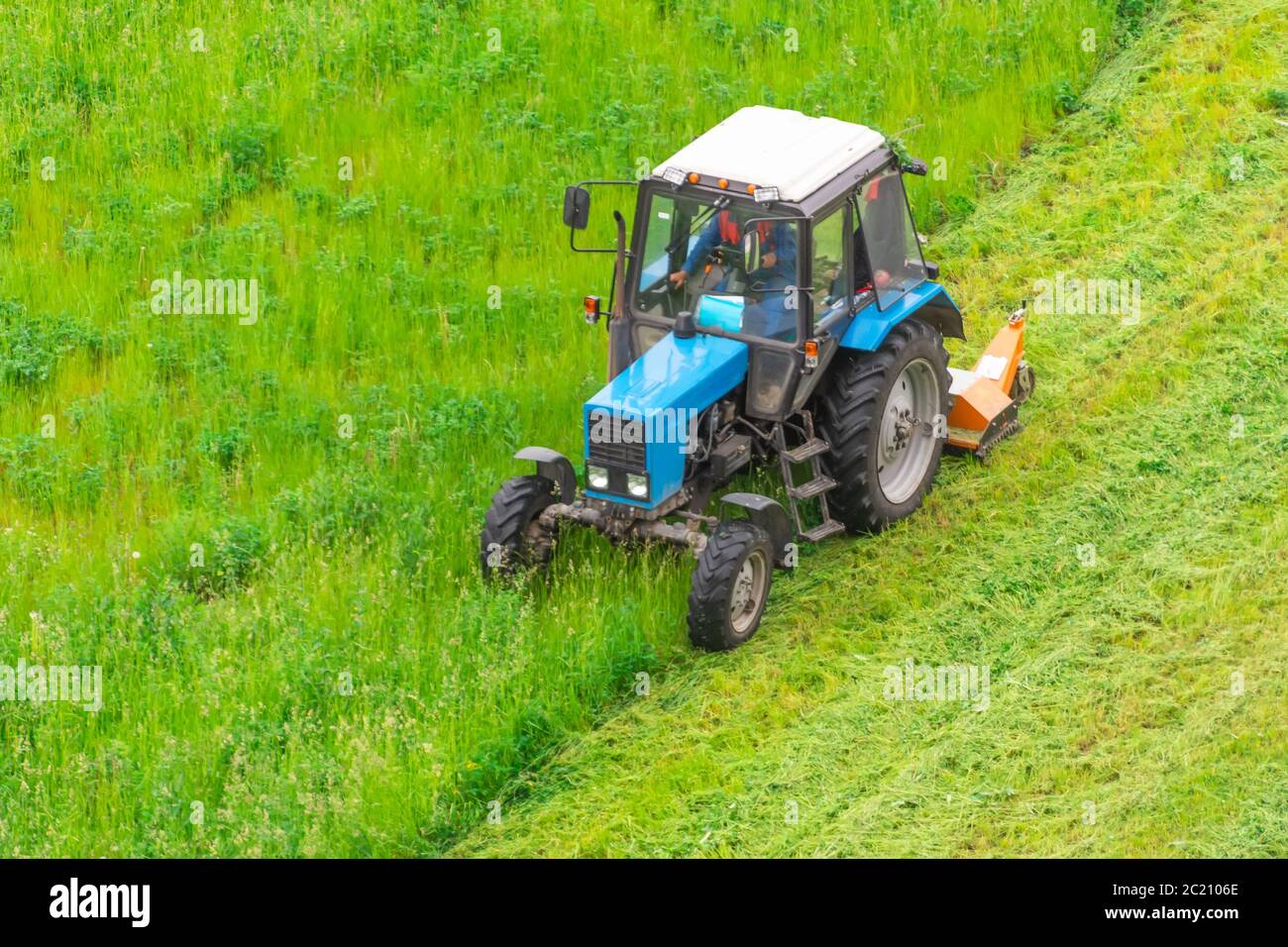 Il trattore utilizza il rasaerba trainato per falciare l'erba sui prati della città, vista aerea Foto Stock
