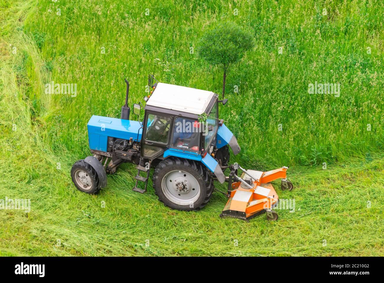 Il trattore utilizza il rasaerba trainato per falciare l'erba sui prati della città, vista aerea Foto Stock