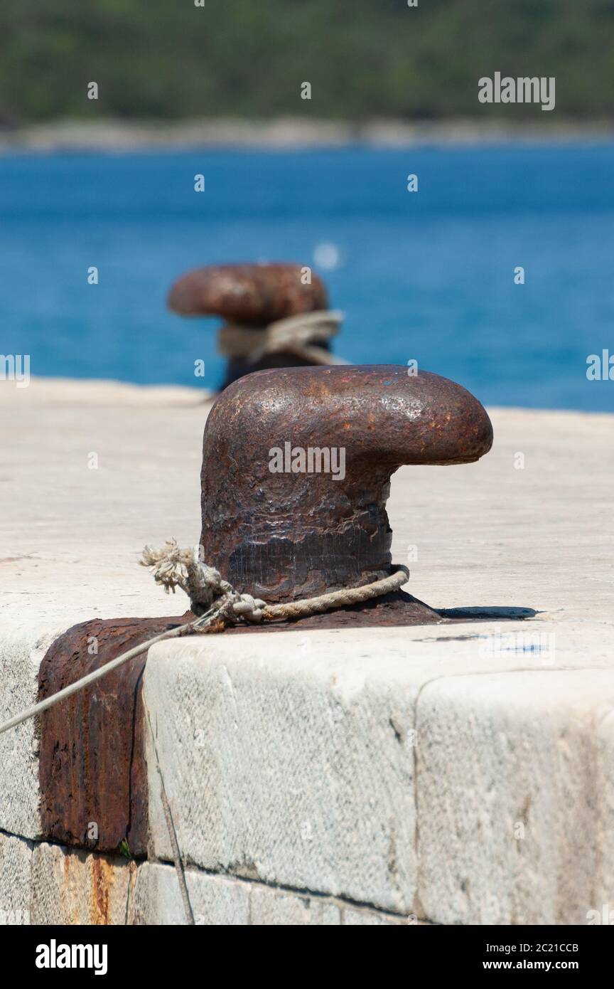 Vecchio e arrugginito paletto ormeggio su molo in cemento con mare blu sullo sfondo. Concetti di vela, vacanza, viaggio, turismo e attività marittime Foto Stock