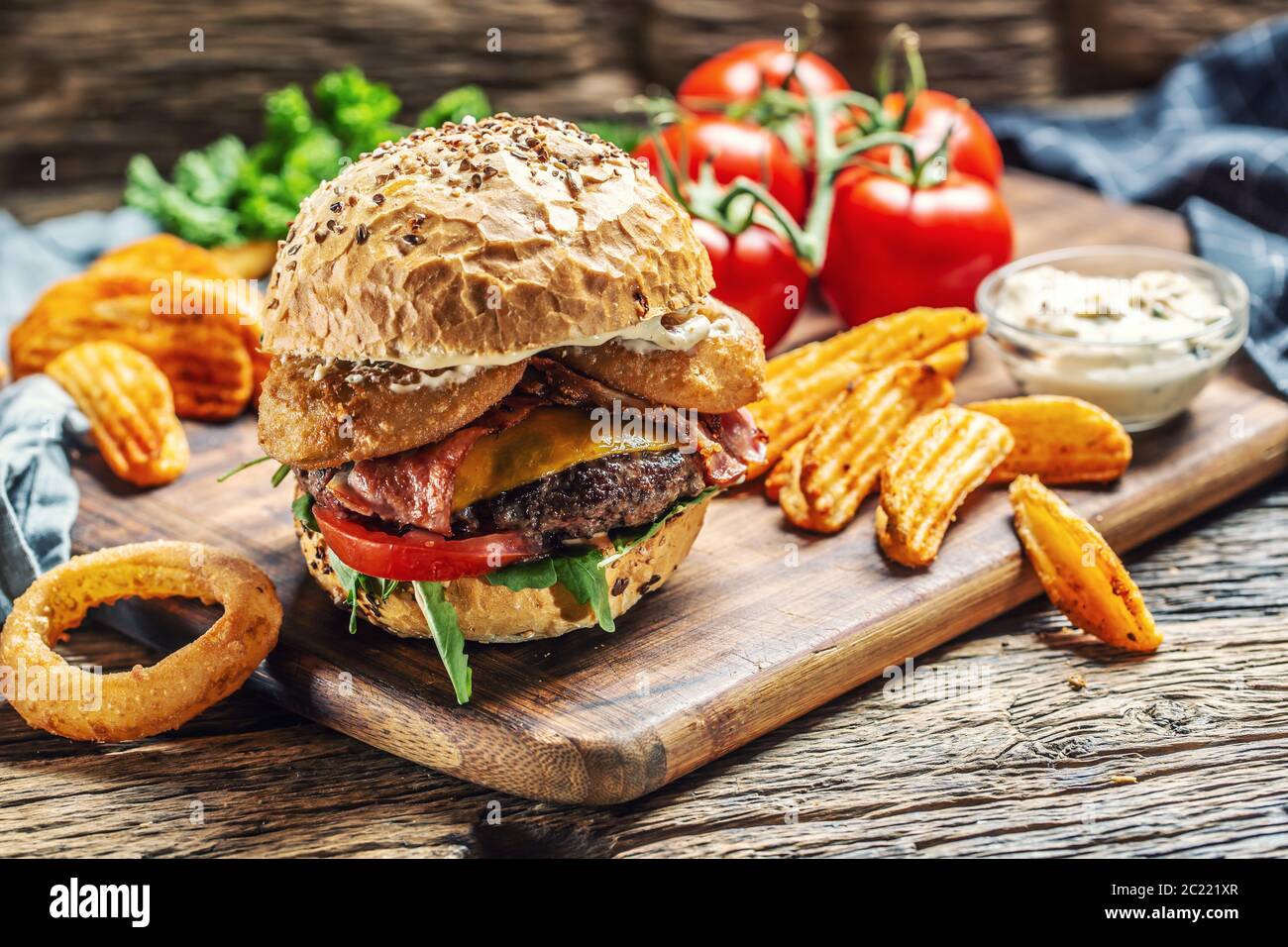 Budrger di manzo con doppio formaggio, spicchi di patate, anello di cipolla, pomodoro, maionese su una scacchiera scura Foto Stock