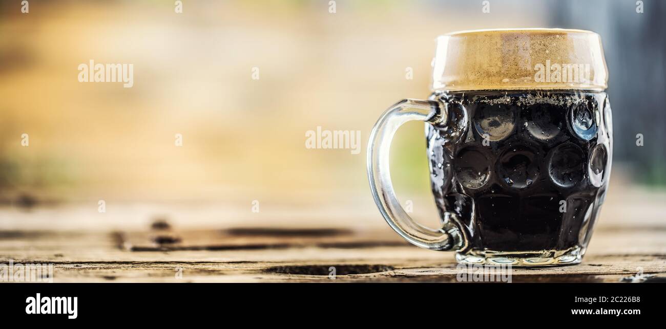 Pinta di birra scura su un tavolo di legno posto sul lato di una fotografia Foto Stock