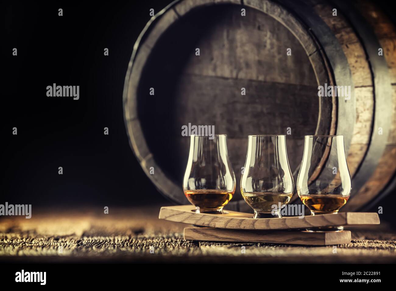Bicchieri per degustazione di whisky Glencairn su una porzione di legno, con un barile di whisky su sfondo scuro Foto Stock