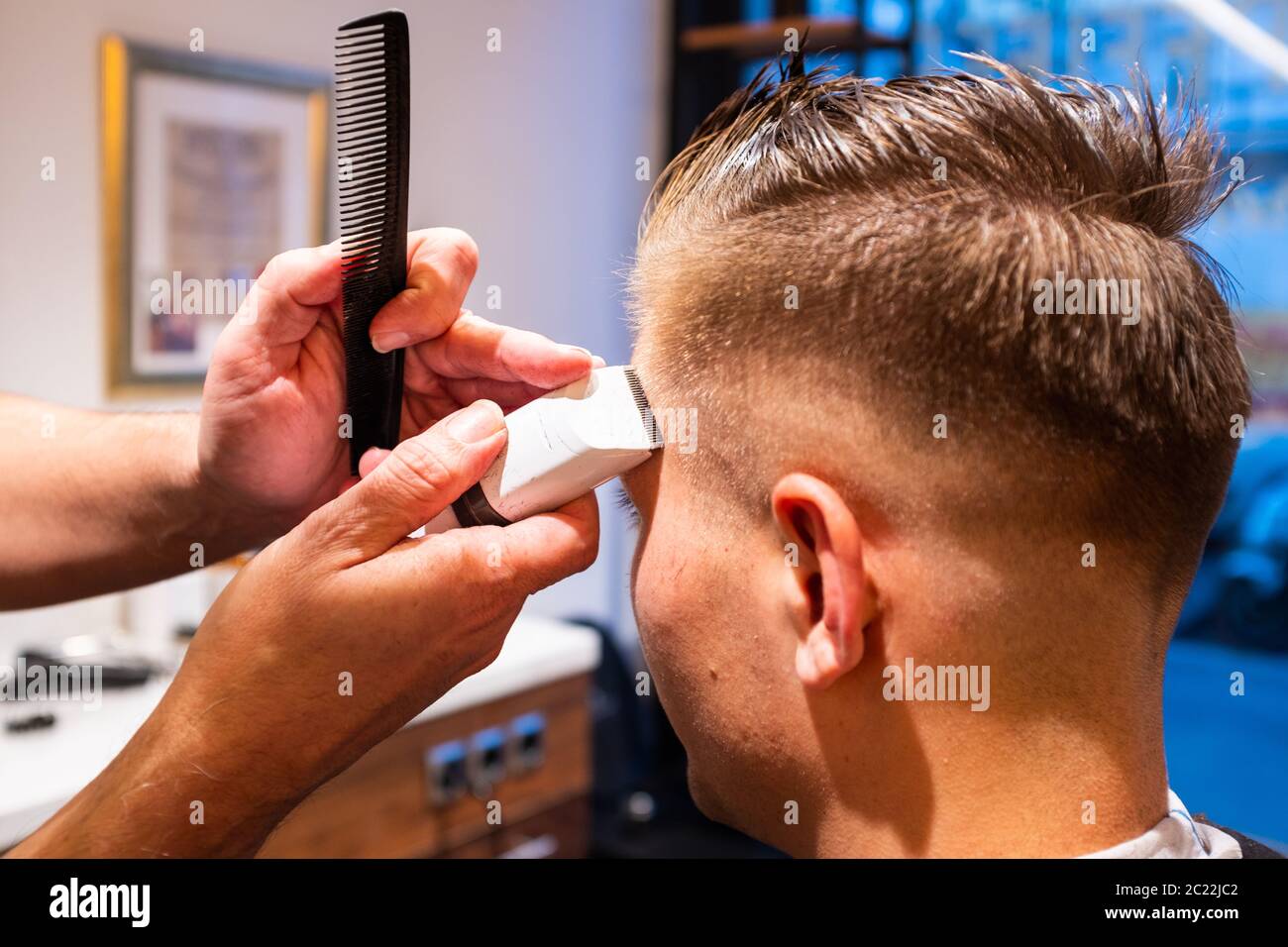 Barber rifinì i capelli di un giovane con un rasoio nel suo barbiere Foto Stock