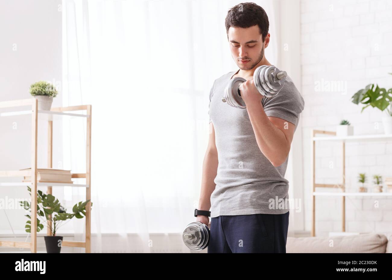 Palestra a casa. Ragazzo con il tracker di fitness tiene i manubri Foto Stock