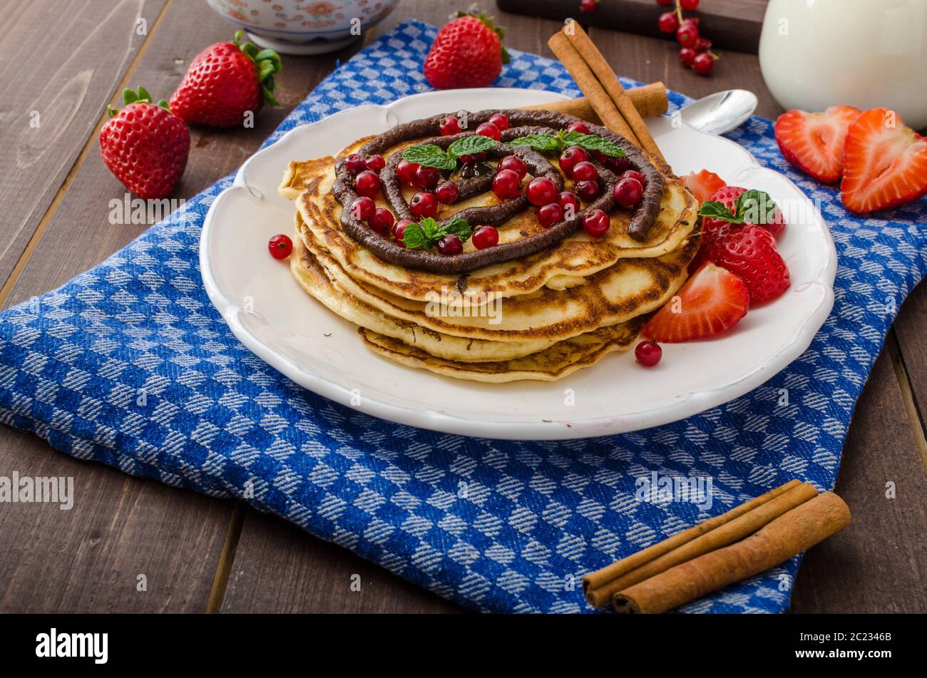 Frittelle di cannella con salsa di cioccolato e frutti di bosco, latte fresco e fragole Foto Stock