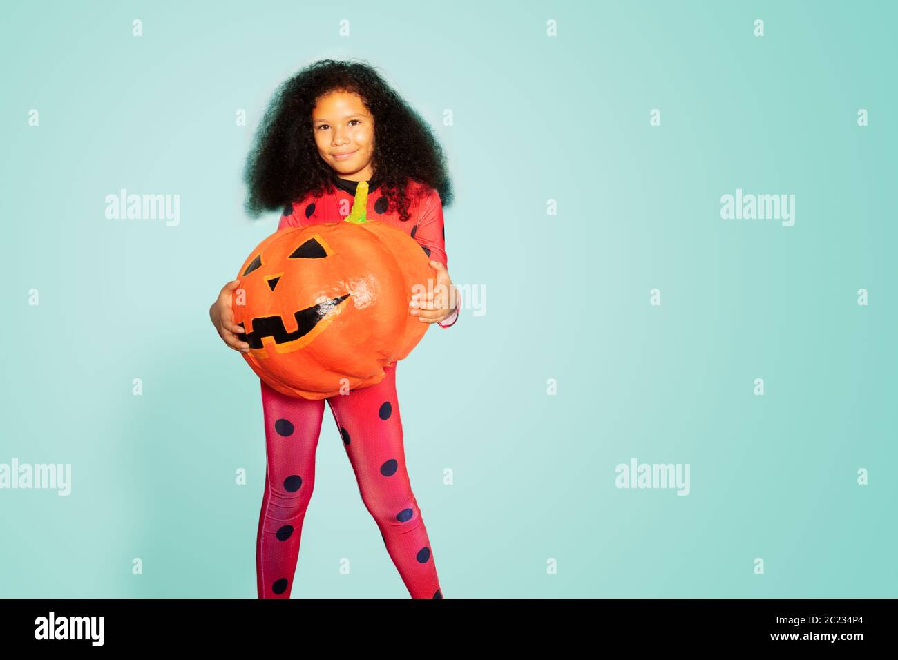Ritratto della ragazza tenere Halloween zucca e sorridere sulla parete blu Foto Stock