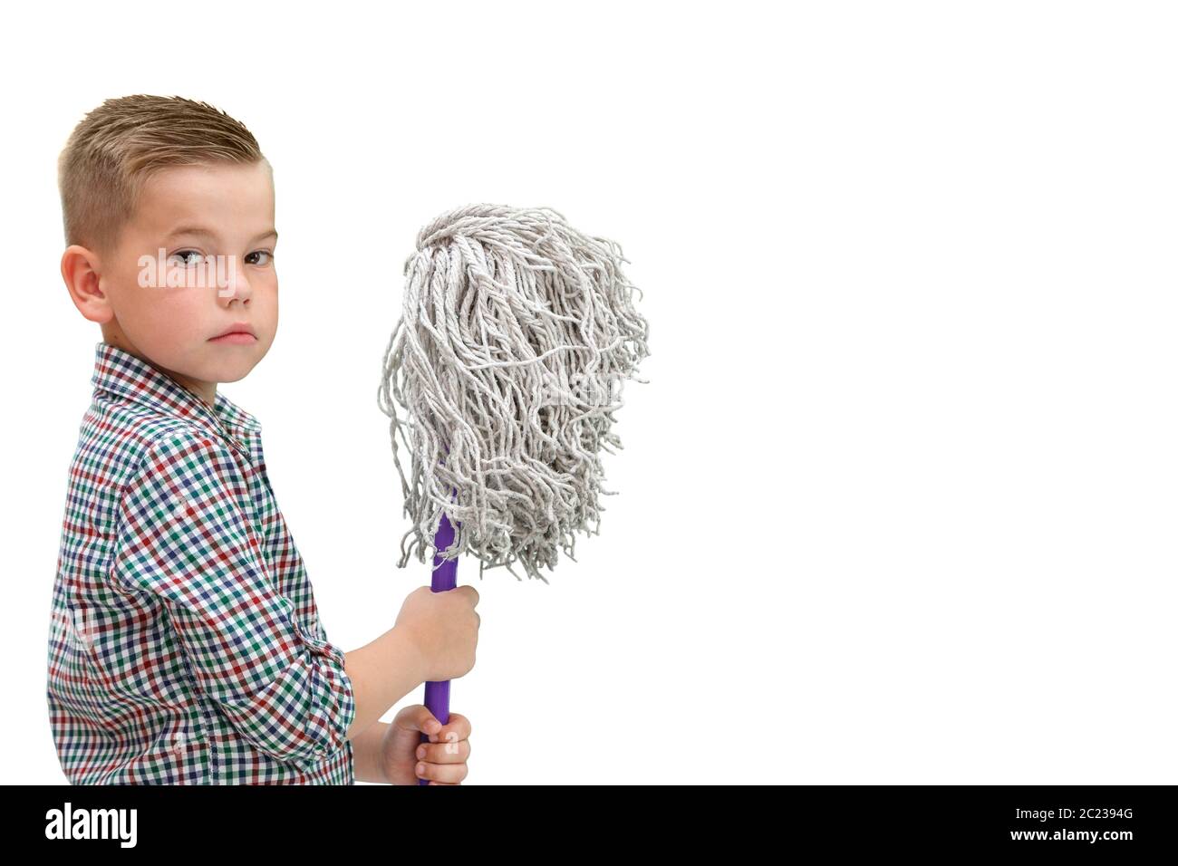 Un piccolo ragazzo calvo in un plaid shirt su un bianco sfondo isolato si erge con un MOP nelle sue mani Foto Stock