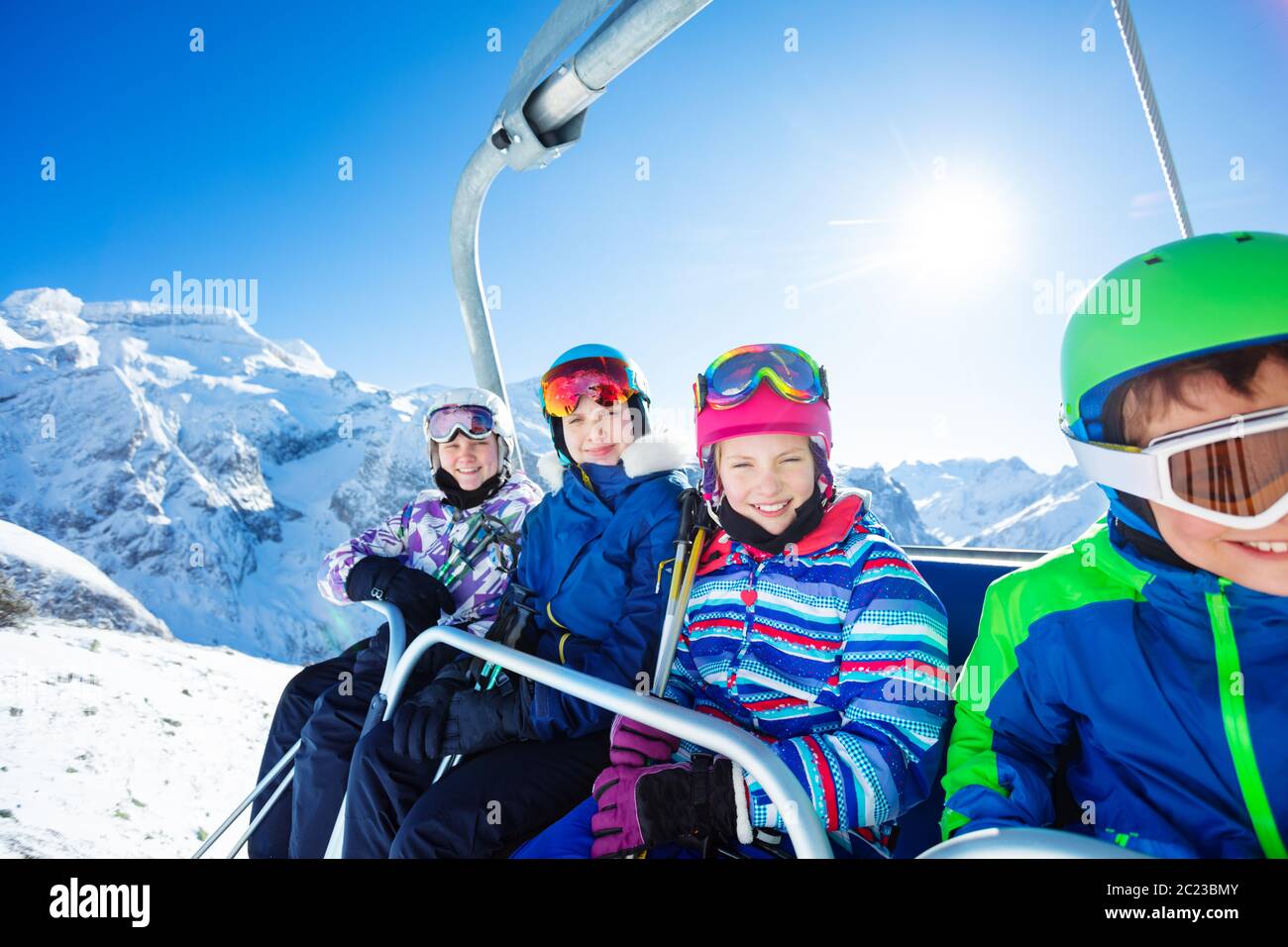 Gruppo di quattro bambini sorridenti si siedono sulla seggiovia insieme alla magnifica e bella vetta di montagna in giornata di sole Foto Stock