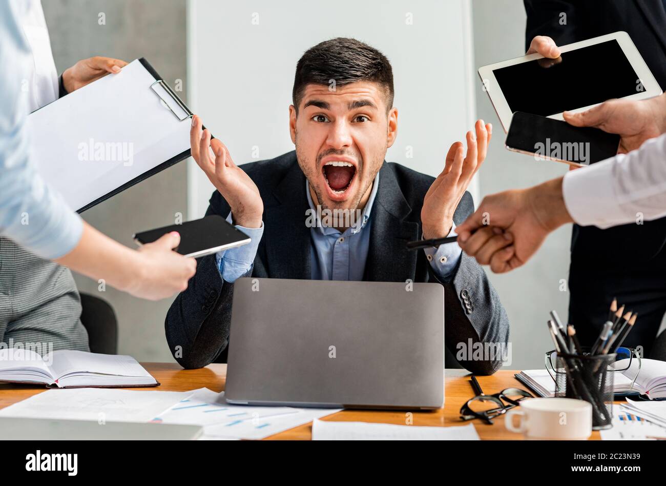 Uomo d'affari gridando sottolineato da più compiti seduti in ufficio moderno Foto Stock