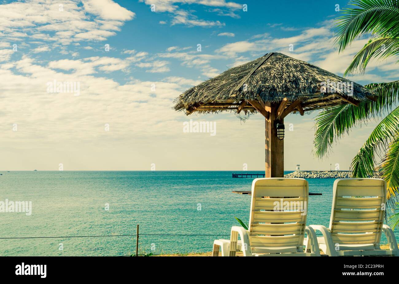 Spiaggia tropicale paesaggio con sedie a sdraio e ombrelloni sulla sabbia vicino al mare in una bella giornata di sole. Scenic acqua e pier background a resort. C Foto Stock