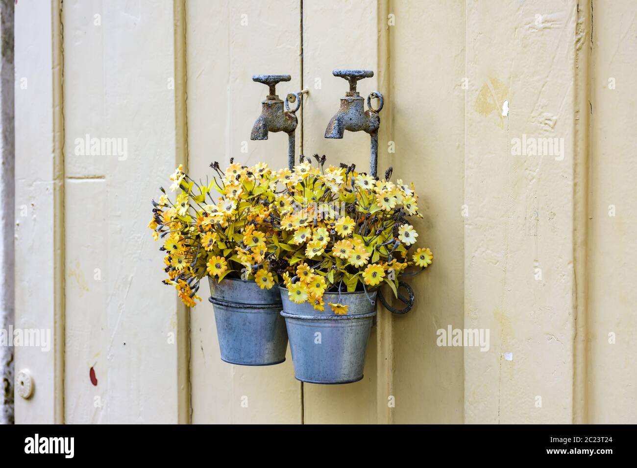 Secchio con fiori appesi su un vecchio rubinetto Foto Stock