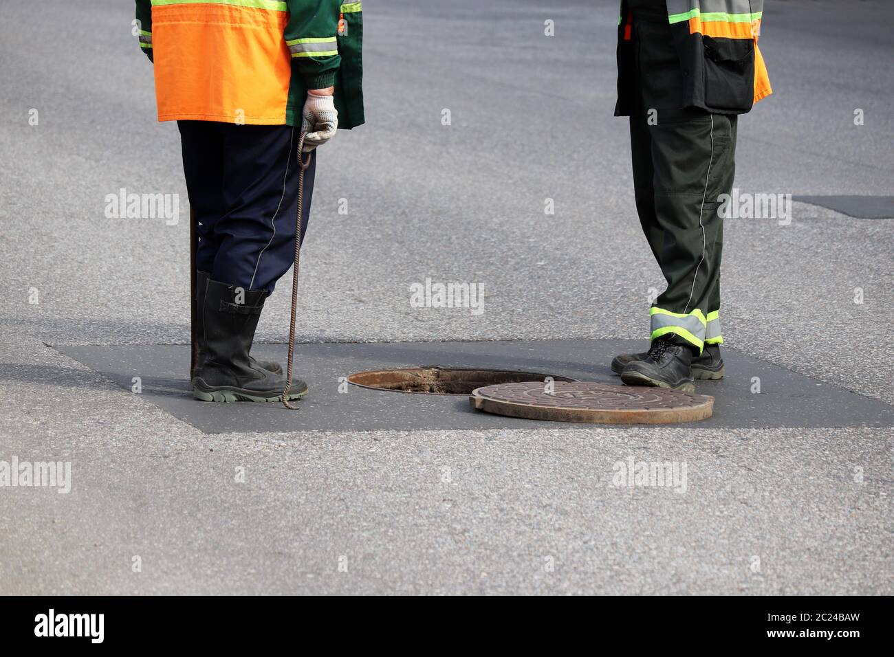 Lavoratori sopra il portello aperto della fogna su una strada. Concetto di riparazione di acque reflue, servizi sotterranei, impianti di alimentazione idrica, posa di cavi Foto Stock