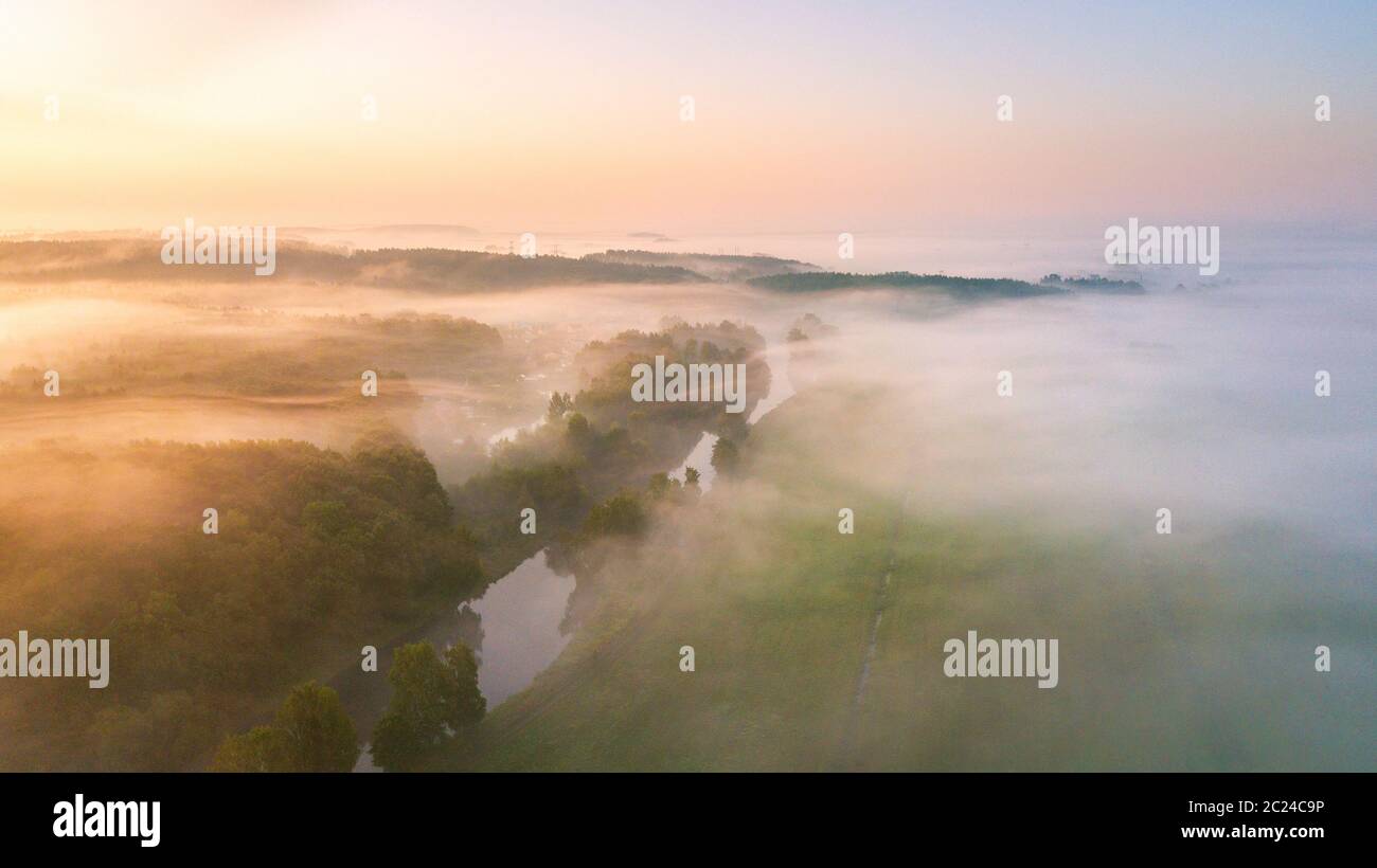 Estate natura paesaggio panorama dell'antenna. Nebbia di mattina su fiume, prato e bosco. Una natura che stupisce la luce del sole di scena a foggy sunrise. La Bielorussia, Europa Foto Stock