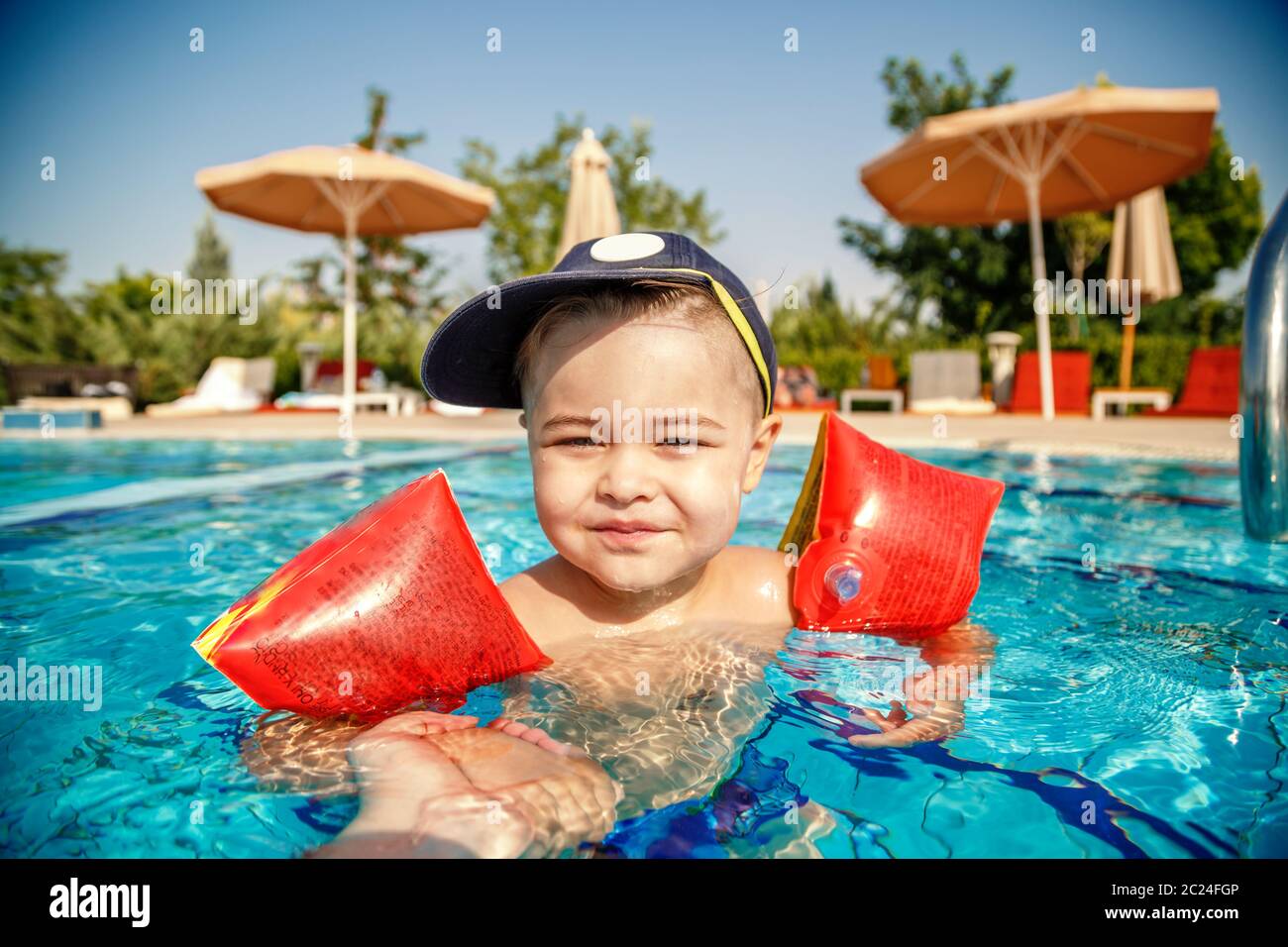 Un piccolo ragazzo impara a nuotare in piscina in estate con il sostegno di suo padre le mani Foto Stock