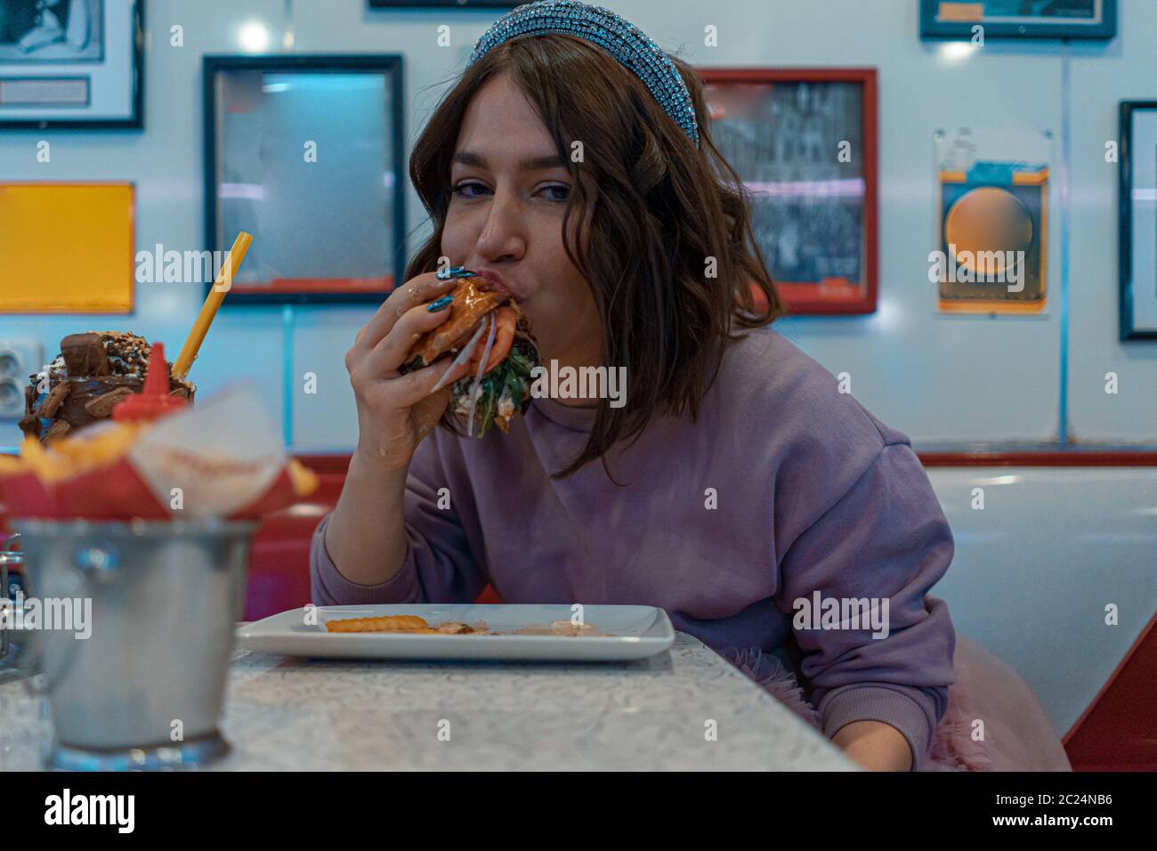 Affamato attraente Donna appetitosamente mangiare Burger all'American Cafe. Gusterete un pasto caldo. Fast food americano Foto Stock