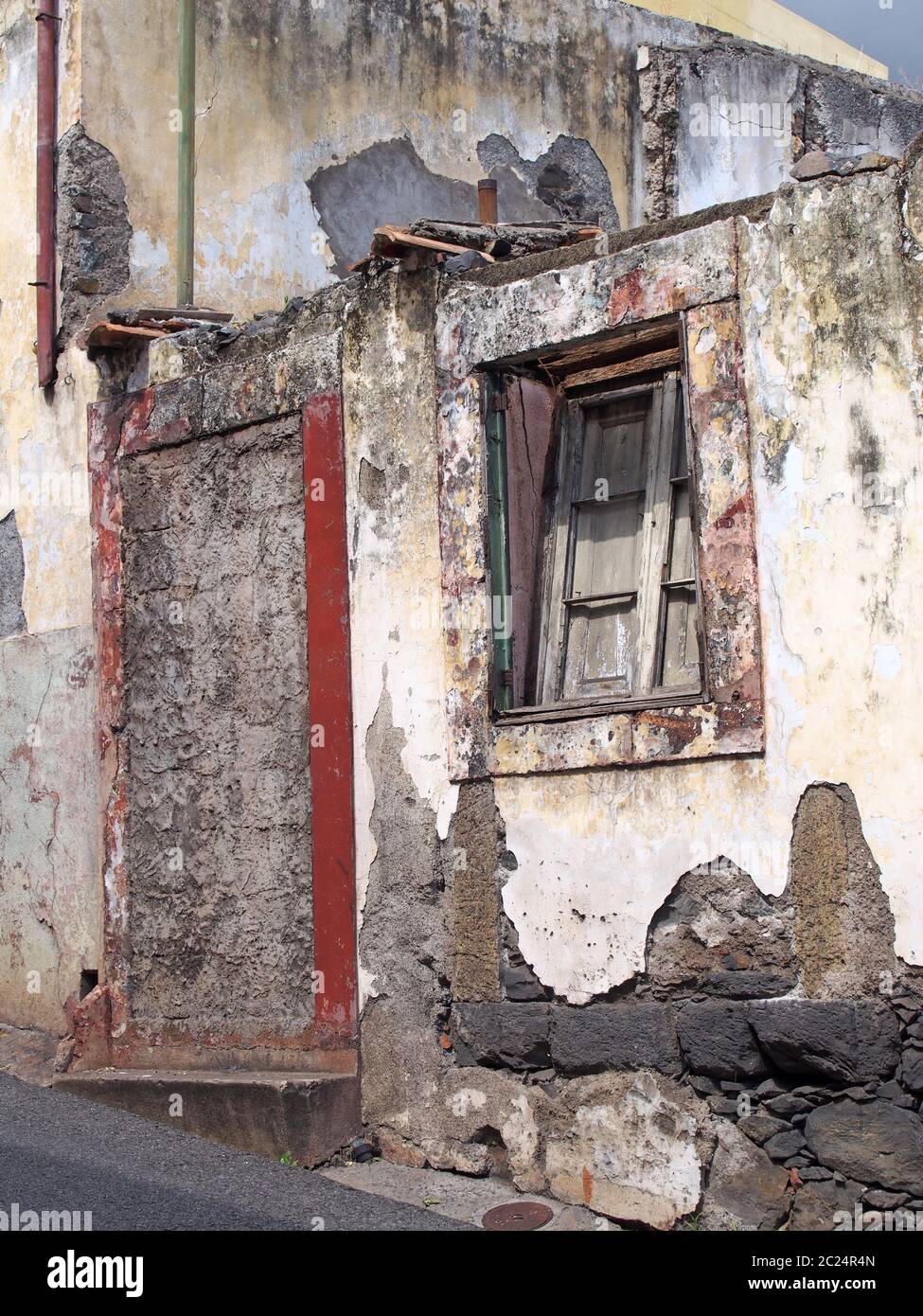 una vecchia casa in rovina in parte crollò su una strada in pendenza con una porta bloccata che sbriciola le pareti e sbiadisce le finestre dipinte di rosso Foto Stock