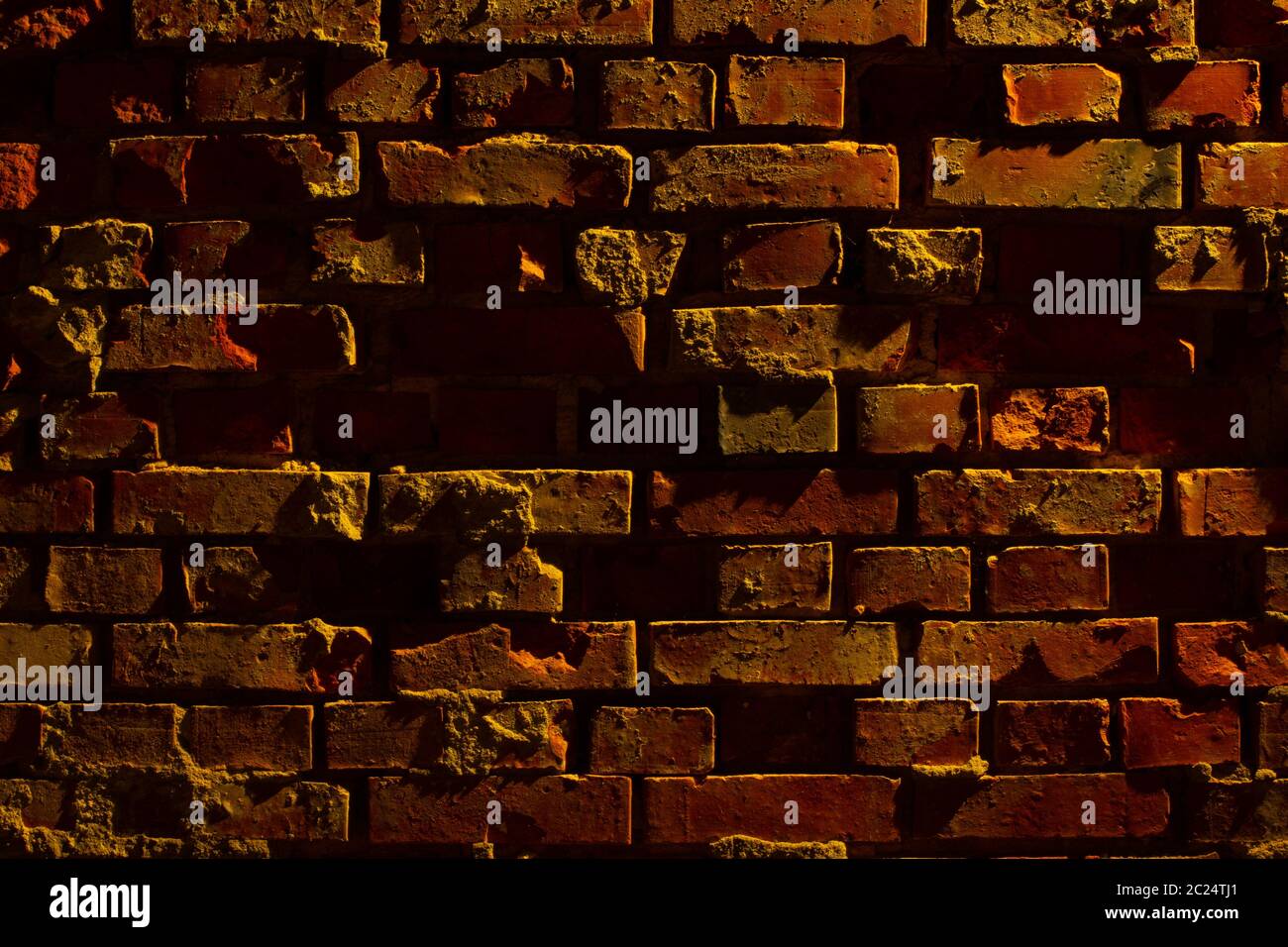 Vecchia grugia e muro di mattoni rossi danneggiato di notte con luce di una lanterna che splende su di essa Foto Stock