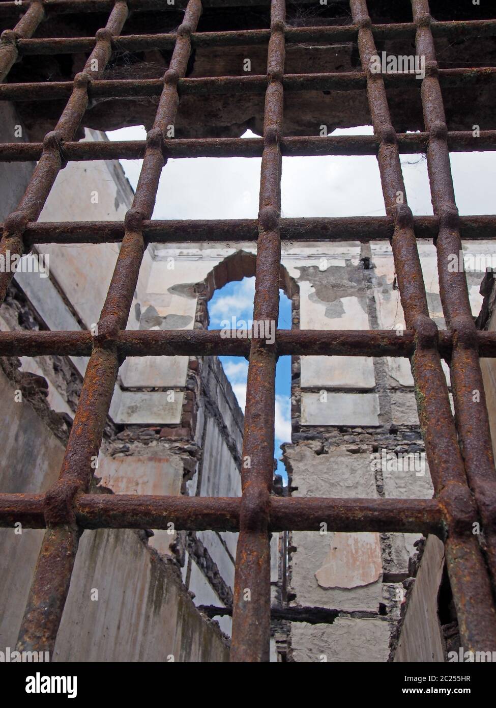 vista attraverso le ruste barre di ferro su una finestra di un edificio in  rovina collassante con pareti sbriciolanti e aperto al cielo Foto stock -  Alamy