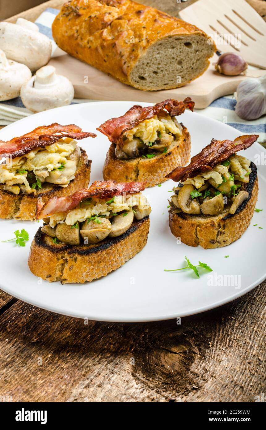 La colazione in stile rustico - aglio toast fritti, funghi, uova strapazzate e pancetta sulla parte superiore Foto Stock