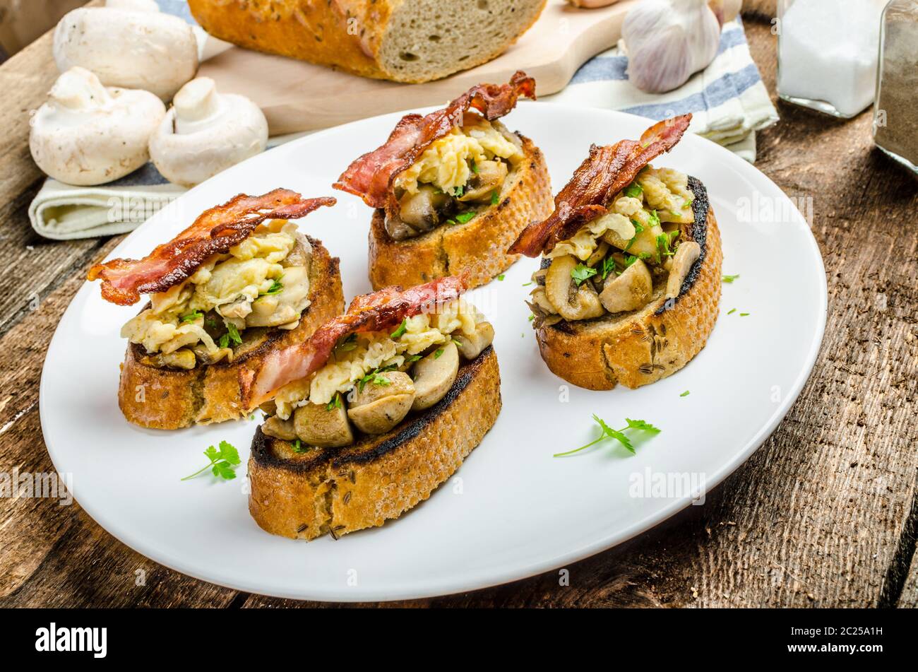 La colazione in stile rustico - aglio toast fritti, funghi, uova strapazzate e pancetta sulla parte superiore Foto Stock