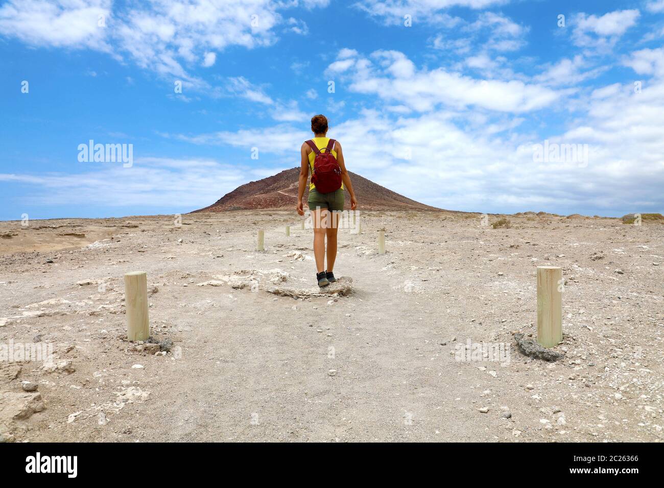 Giovane donna degli escursionisti a piedi nel percorso verso la montagna rossa contro il cielo blu con nuvole bianche in Tenerife. Angolo basso. Foto Stock