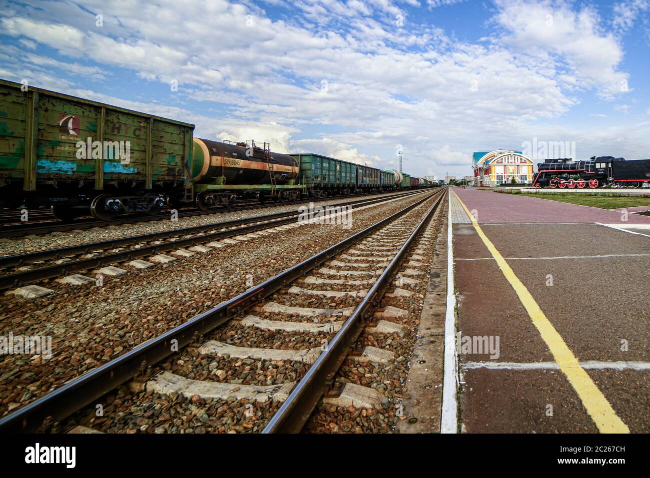 Vista dei binari ferroviari lungo la piattaforma, andando in lontananza. Cielo con nuvole Foto Stock