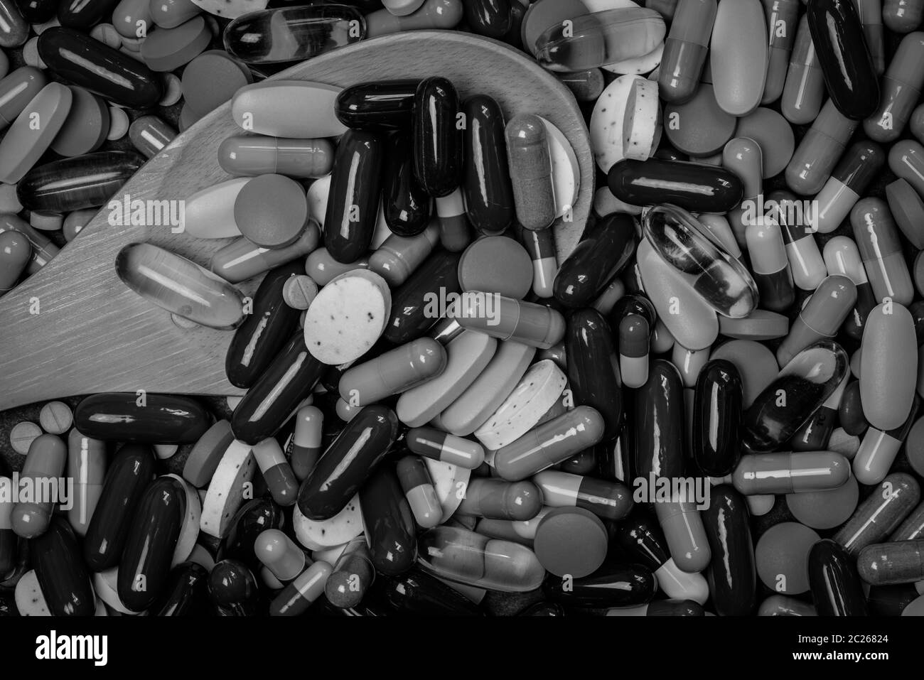 Molti di capsule e compresse pillole e cucchiaio di legno in immagine in bianco e nero. Un uso eccessivo di farmaci e concetto di sovradosaggio. Il consumo di stupefacenti nelle persone anziane con chron Foto Stock