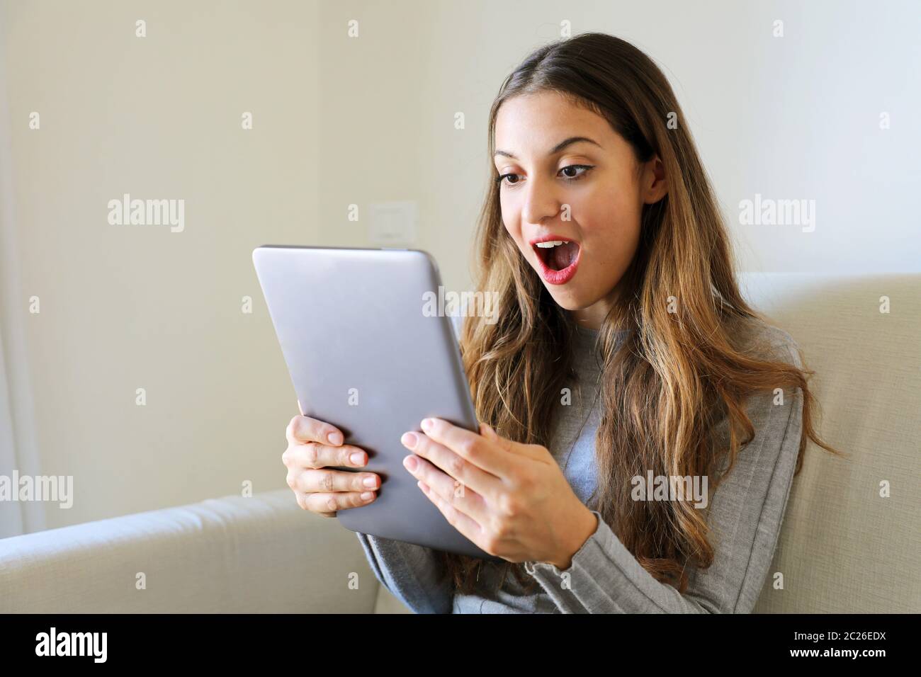 Ragazza felice che usa il tablet. Donna entusiasta che tiene il tablet pc sul divano a casa Foto Stock