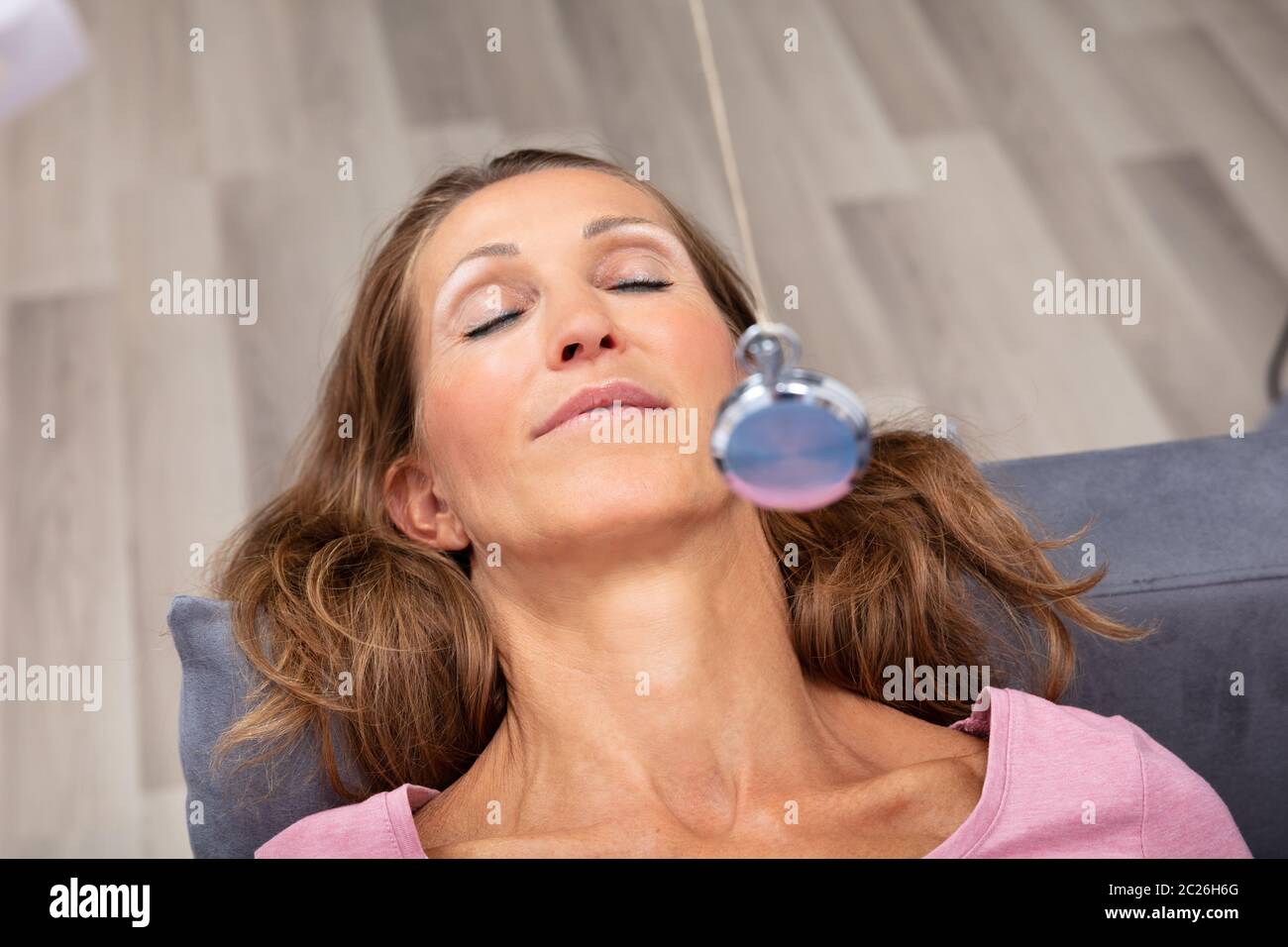 Attraente donna matura essendo ipnotizzato mentre sdraiato sul divano Foto Stock