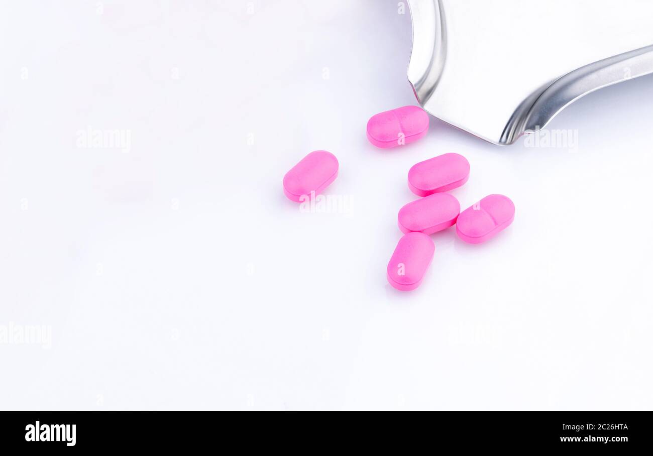 Pila di compresse di colore rosa confetto su sfondo bianco nei pressi di acciaio inossidabile farmaco vassoio. Norfloxacin 400 mg per il trattamento la cistite. Antibiotici la resistenza al farmaco. Foto Stock