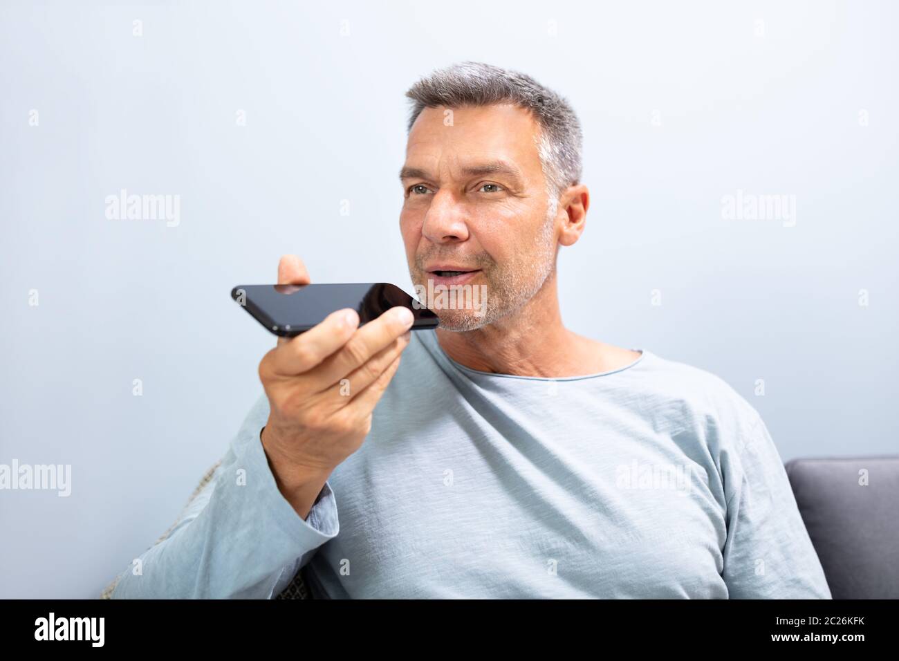 Close-up di una barba uomo con funzione di riconoscimento vocale sul proprio telefono cellulare contro uno sfondo bianco Foto Stock