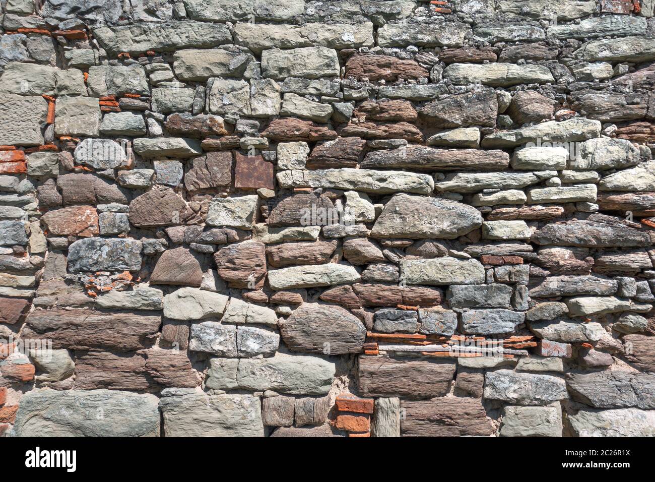 Vecchio muro di pietra ruvida con pietre molto diverse alla luce del sole Foto Stock