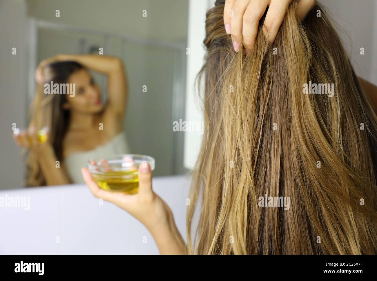 Giovane donna di applicare olio d'oliva maschera su capelli davanti ad uno specchio. Cura dei capelli concetto. Focus sui capelli. Foto Stock