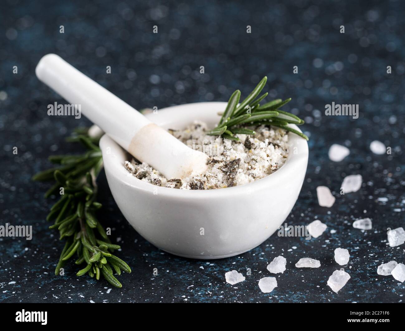 Primo piano vista su mortaio e pestello con rosmarino profumato sale marino e scorza di limone. Rosmarino di erbe profumate al sale marino su sfondo blu scuro. Sale profumato Foto Stock