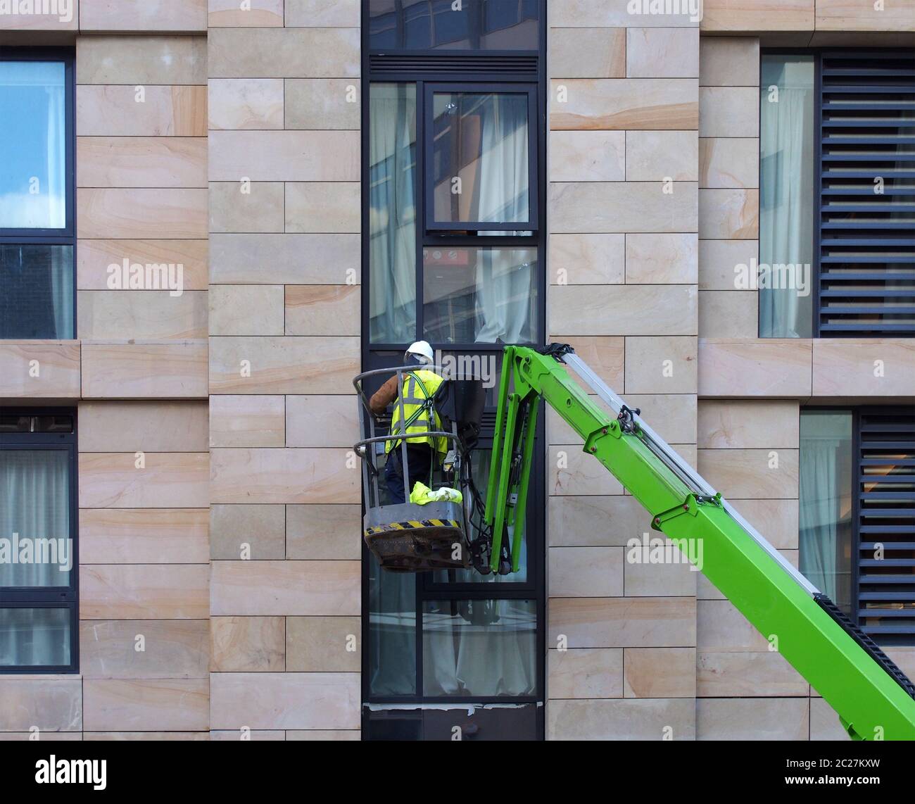 un operatore di costruzione non identificabile in una piattaforma di lavoro aerea verde su un grande cantiere urbano di alloggiamento Foto Stock