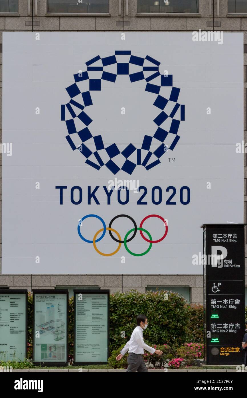 Un salarista giapponese passa davanti all'edificio del governo metropolitano di Tokyo con il logo per le Olimpiadi di Tokyo del 2020, Shinjuku, Tokyo, Giappone Foto Stock