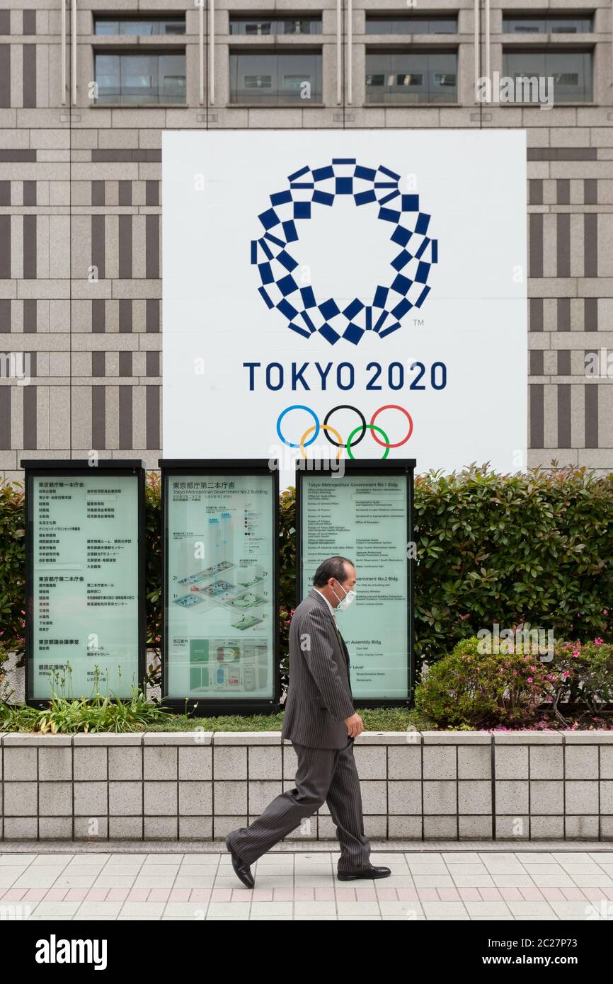 Un salarista giapponese passa davanti all'edificio del governo metropolitano di Tokyo con il logo per le Olimpiadi di Tokyo del 2020, Shinjuku, Tokyo, Giappone Foto Stock
