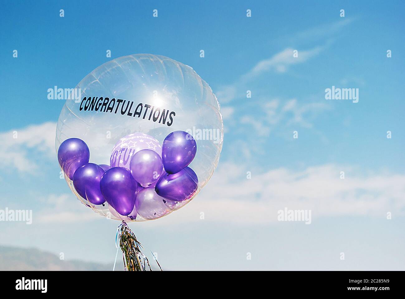 Palloncini viola in grande mongolfiera congratulazioni sul cielo blu con soffici cloud Foto Stock