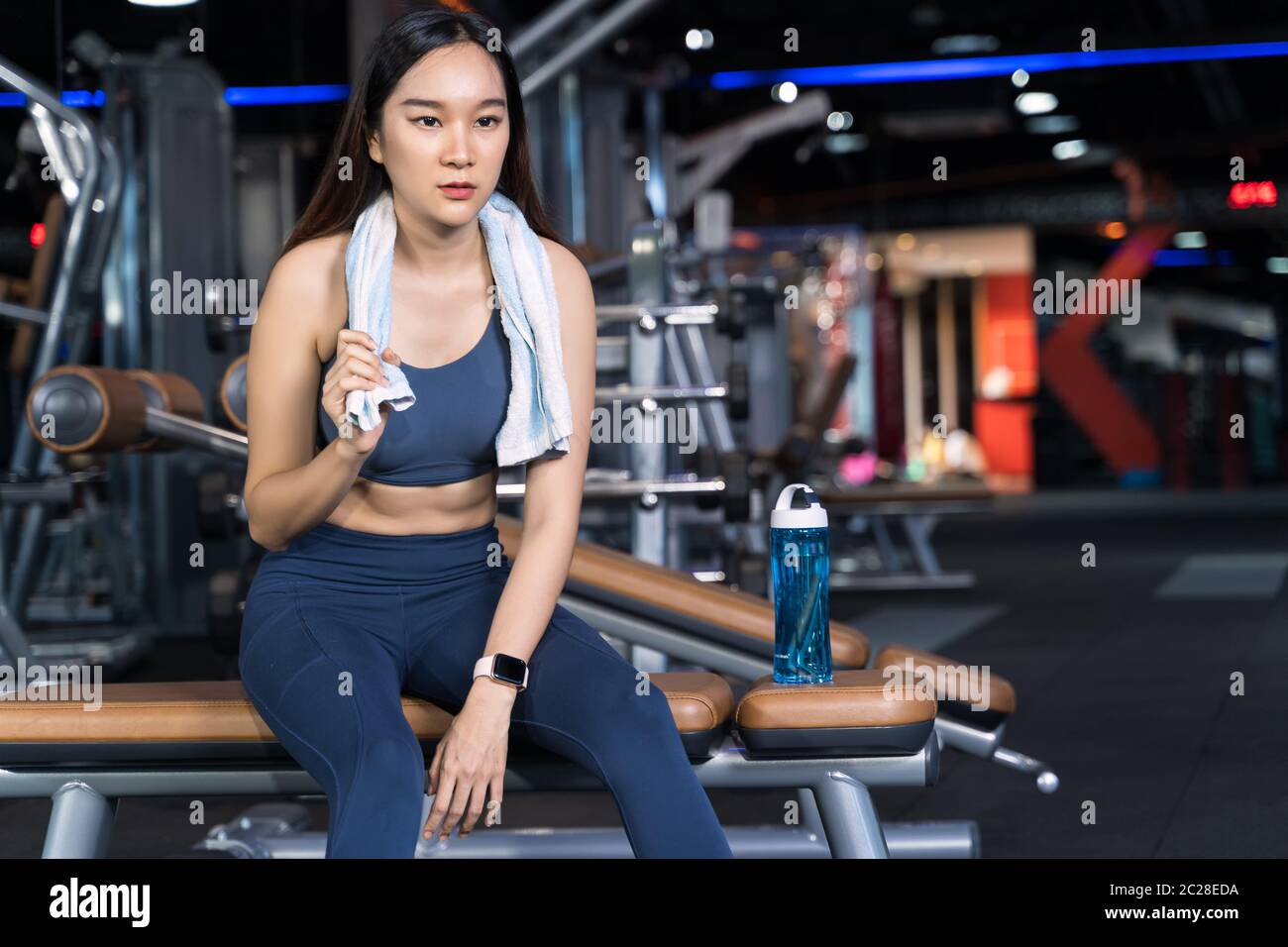 Le donne asiatiche sono sedute sull'esercitazione e stanno tenendo gli asciugamani con le bottiglie dell'acqua poste sui loro lati. È seduta da sola in palestra in healt sportivo Foto Stock