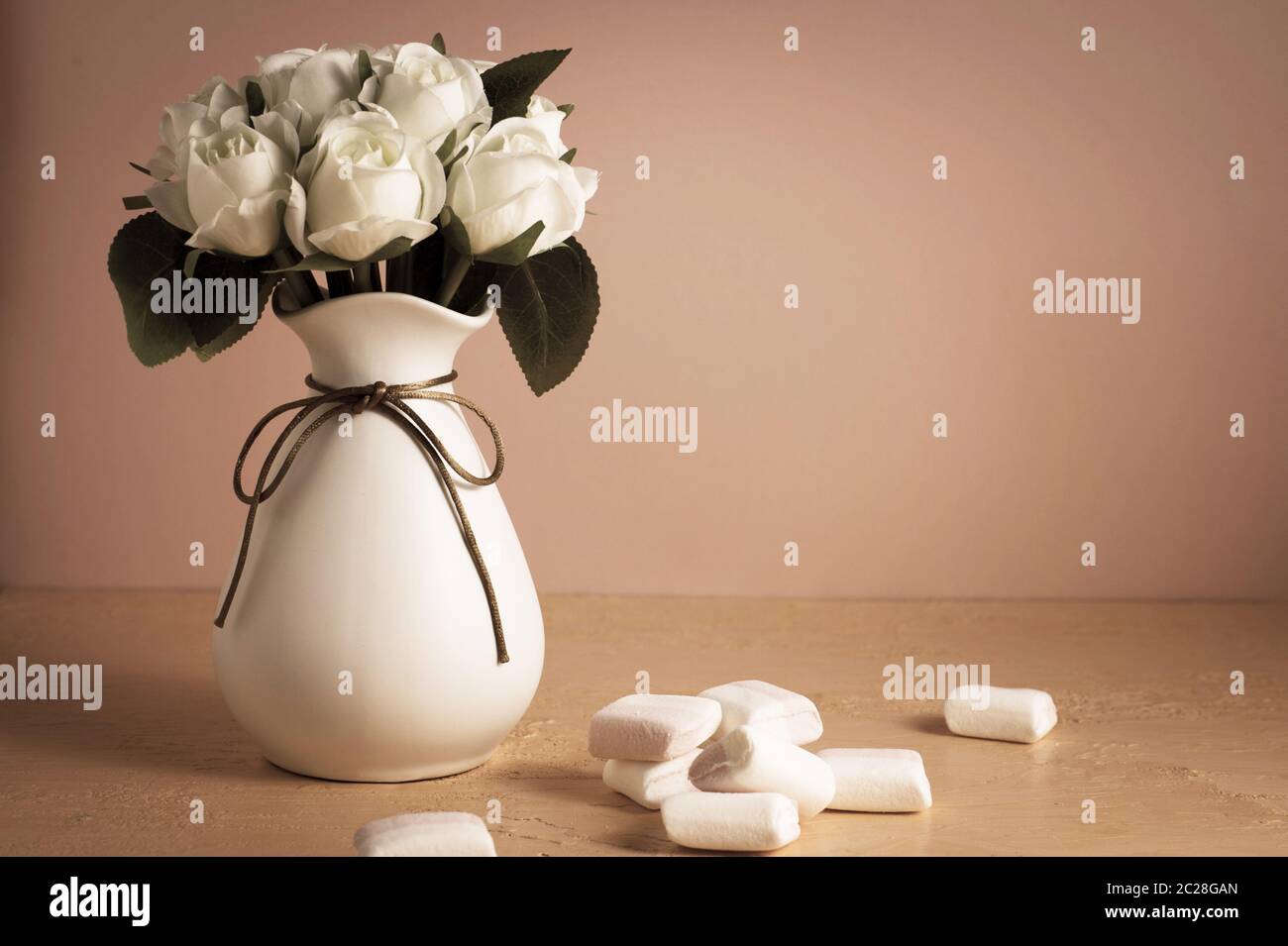 CopySpace con mini marshmallow colorati su un tavolo accanto a rose bianche su sfondo rosa. Foto Stock