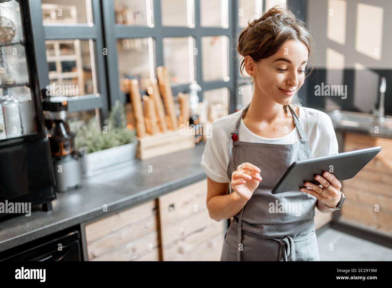 Giovane venditore che lavora con un tablet digitale al banco di un bar o di un negozio di dolciumi. Concetto di piccola impresa e tecnologie nel campo dei servizi Foto Stock