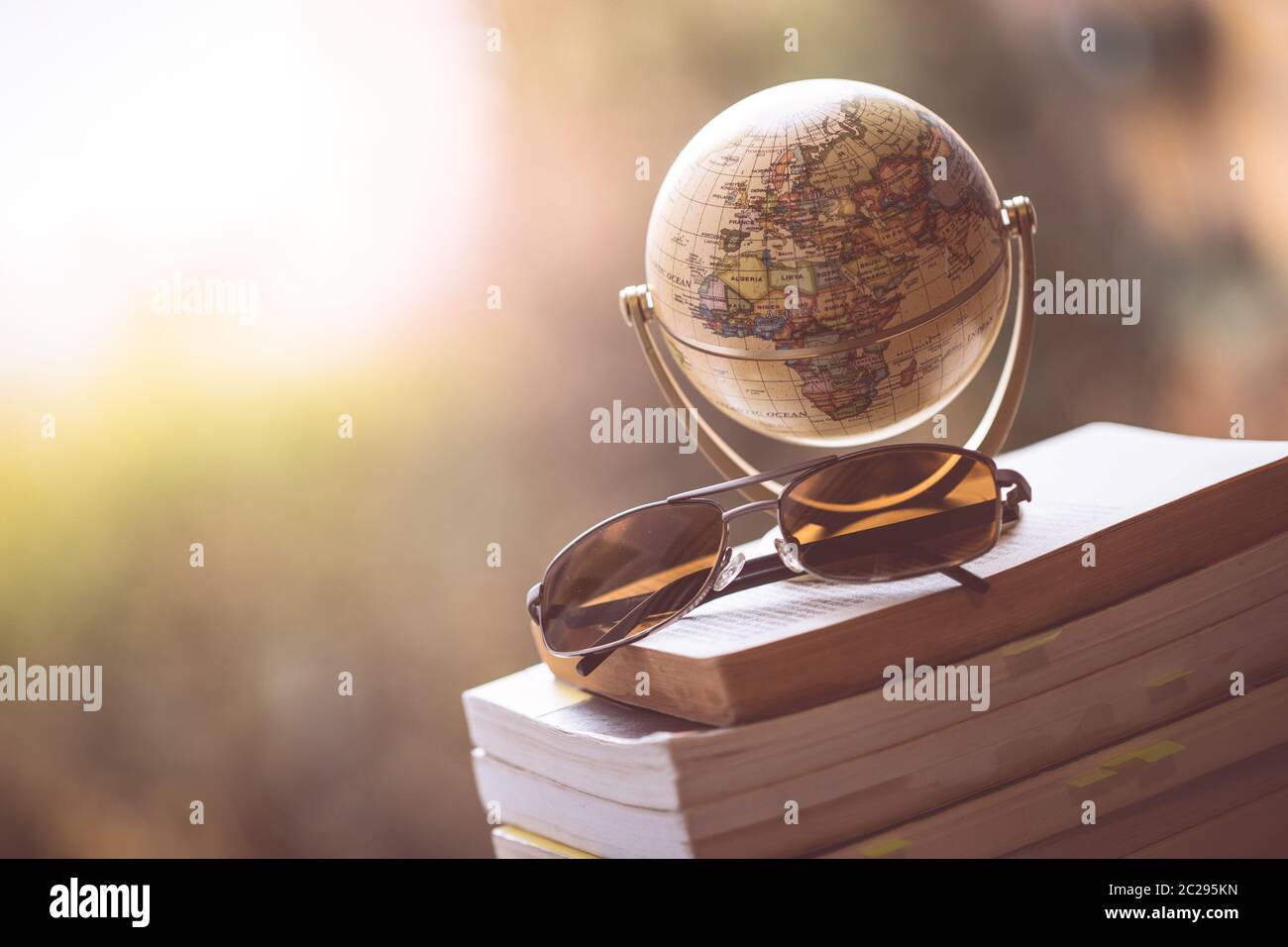 Pianificazione del prossimo viaggio: Globo in miniatura e occhiali da sole su una pila di libri. Foto Stock